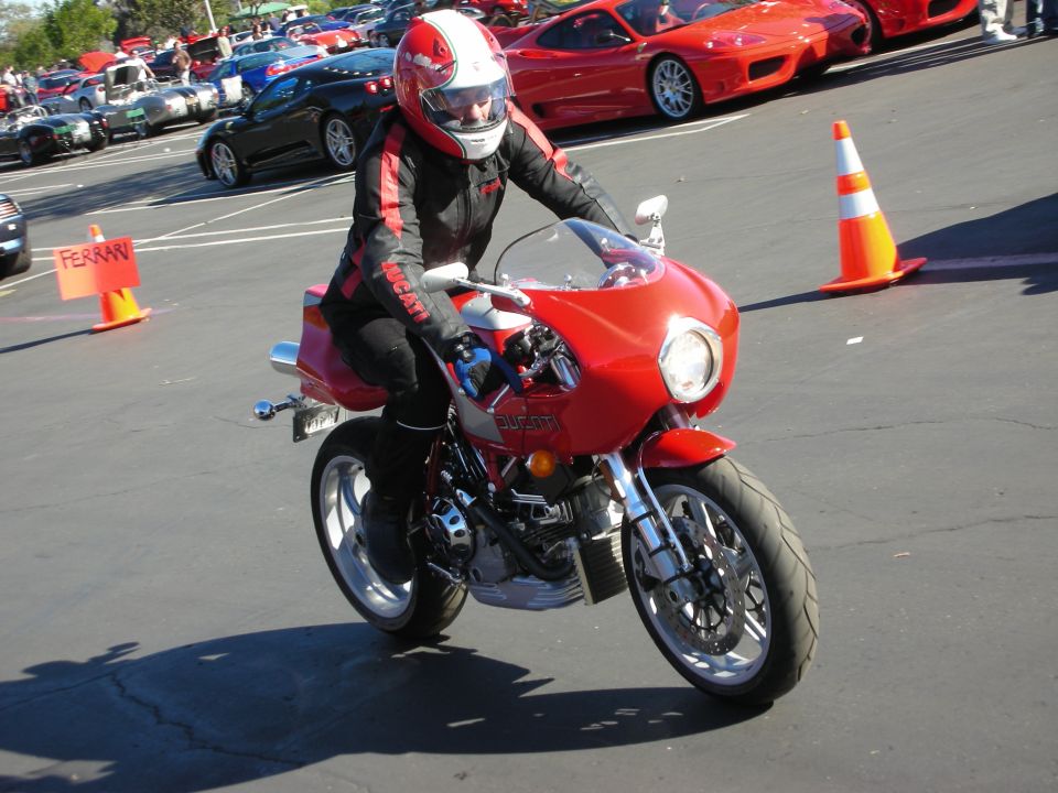 Rider on a red Ducati motorcycle, with red Ferraris in the background