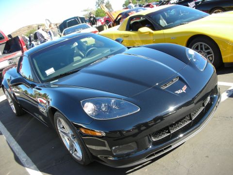 1992 Ford Crown Victoria - A black Chevrolet Corvette is parked in a lot with other vehicles, including a yellow Corvette.