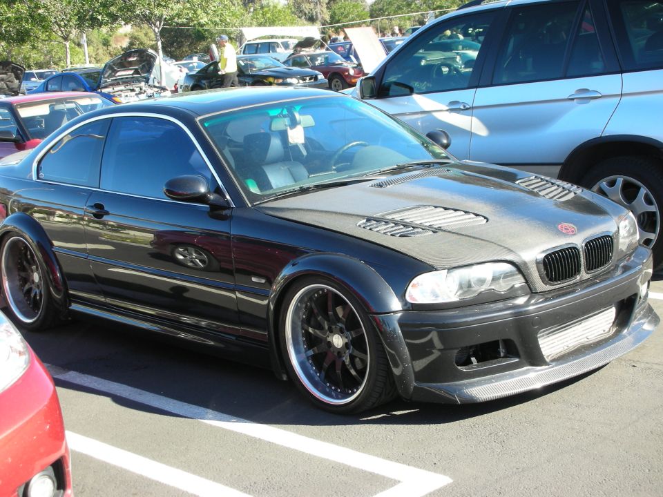 Black coupe with widebody kit, carbon fiber hood with vents, and aftermarket wheels parked in a lot