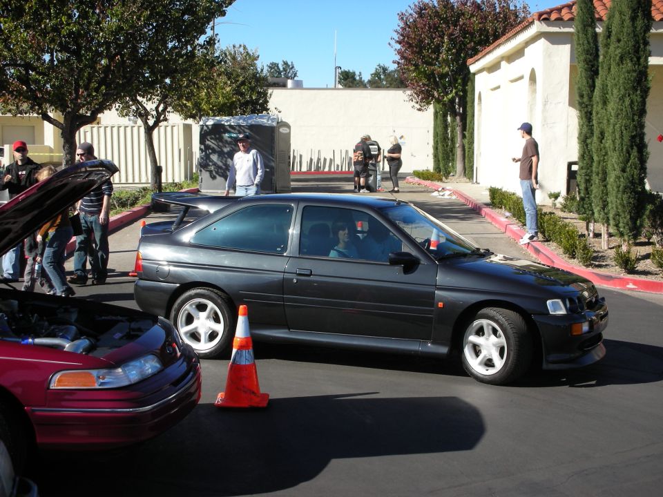 Dark gray hatchback with spoiler parked next to a red car with hood open. People are standing around