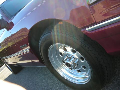 1992 Ford Crown Victoria - A close-up view of a car's wheel and fender shows chrome accents and a dark red paint job.