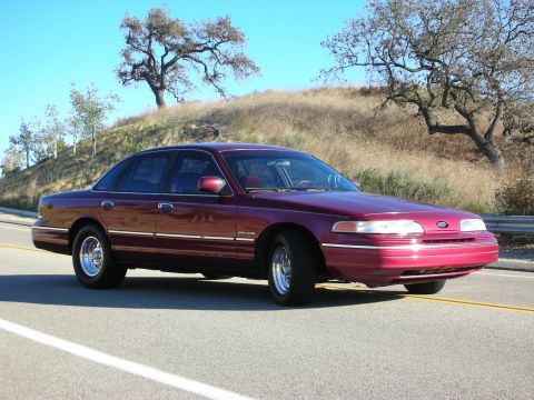 1992 Ford Crown Victoria - 1992 Ford Crown Victoria in a three-quarter front view, parked on a roadside with a natural landscape.