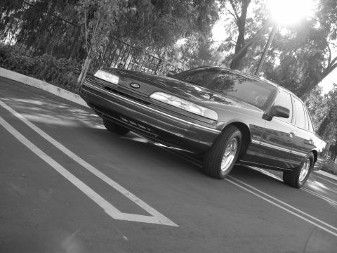 1992 Ford Crown Victoria - A dark 1992 Ford Crown Victoria is captured from a low angle in a parking lot with trees in the background.