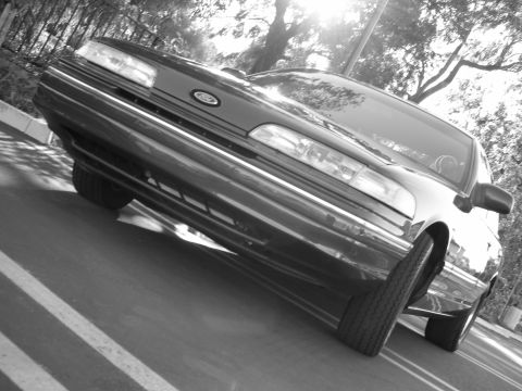1992 Ford Crown Victoria - Front 3/4 view of a 1992 Ford Crown Victoria, captured in black and white with sunlight glinting off the hood.
