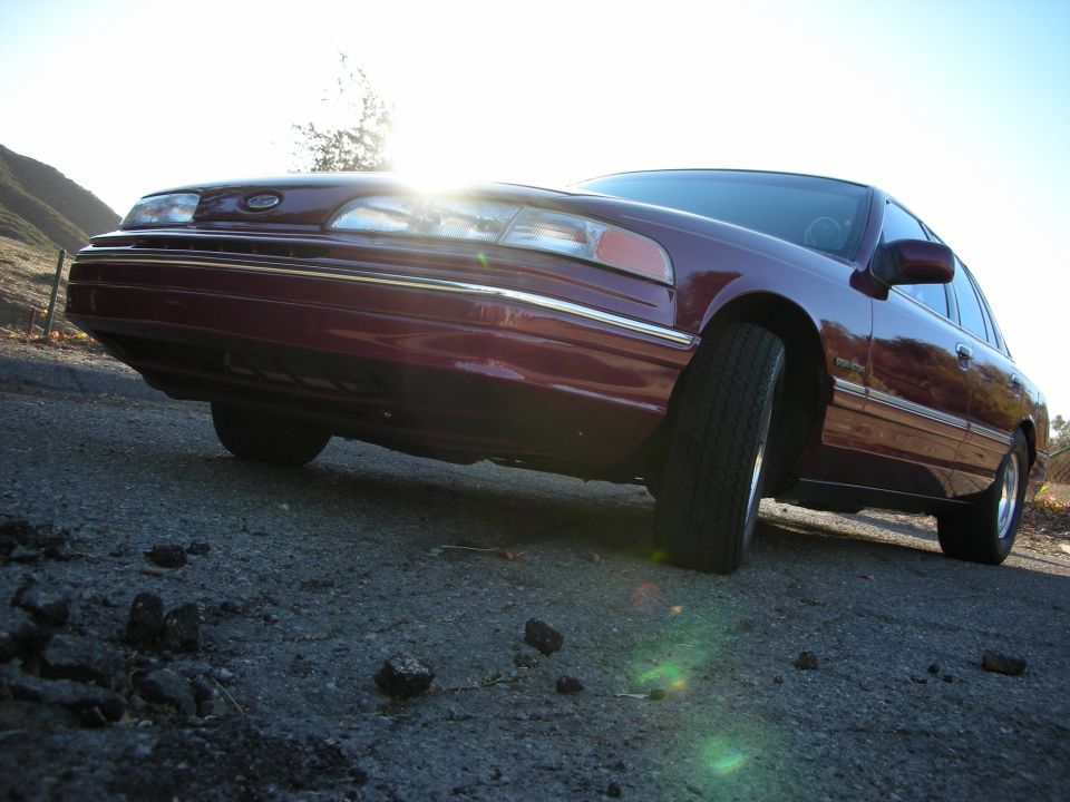 Maroon 1992 Ford Crown Victoria parked on a road with hills in the background