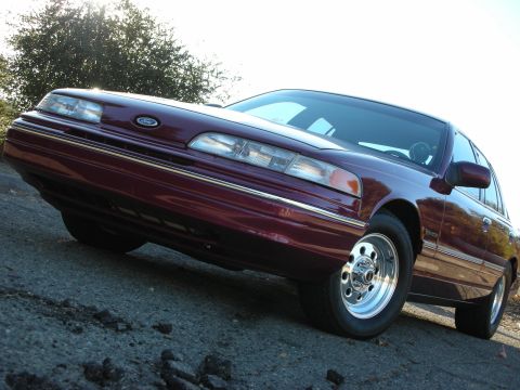 1992 Ford Crown Victoria - A maroon 1992 Ford Crown Victoria sedan is viewed from a low angle, highlighting its front end and side profile.