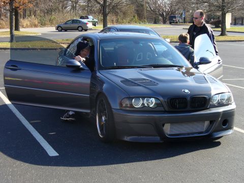 1991 Ford Probe - A dark gray BMW M3 E46 coupe is parked with its driver's door open, showing a front intercooler.