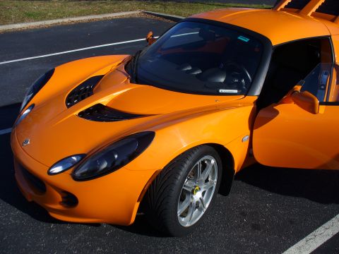1991 Ford Probe - Orange Lotus Elise sports car parked on asphalt, driver's door ajar.