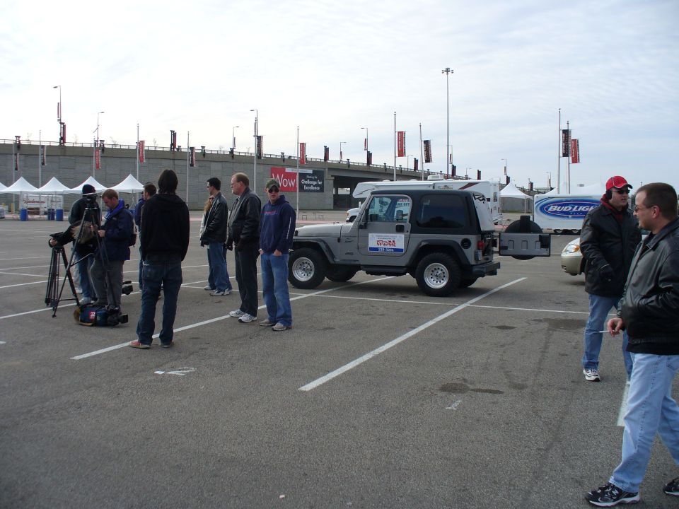 Group of people filming a gray Jeep Wrangler in a parking lot