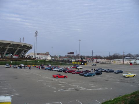 1991 Ford Probe - A variety of vehicles are parked in a lot near a stadium under a cloudy sky.