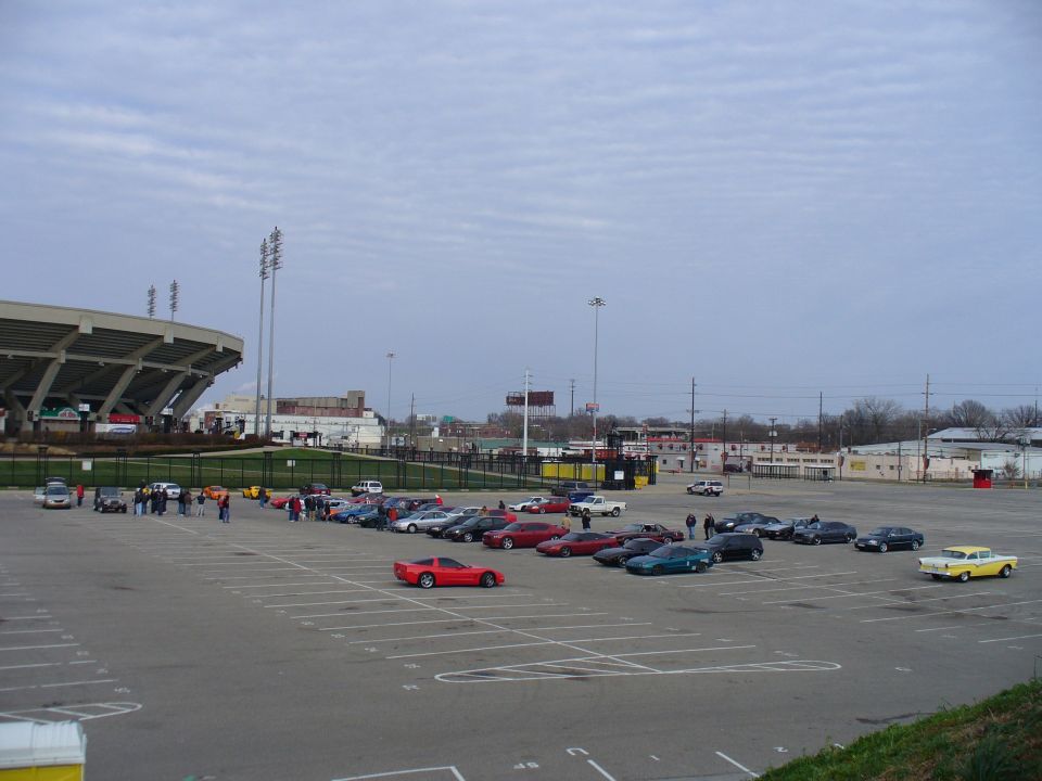 Parking lot with many cars, a stadium, and a yellow classic car