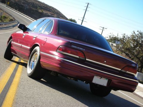 1992 Ford Crown Victoria - The rear of a red 1992 Ford Crown Victoria LX sedan is visible as it drives on a road.