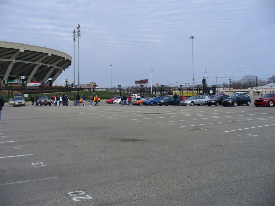 Parking lot scene with a stadium in the background and several cars parked in rows