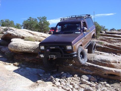 1986 Ford Bronco II - A modified Ford Bronco II navigates a rocky trail under a clear blue sky.