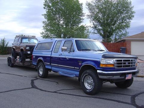 1986 Ford Bronco II - A blue Ford F-250 tows a lifted Bronco II on a trailer, a common practice for off-road enthusiasts.
