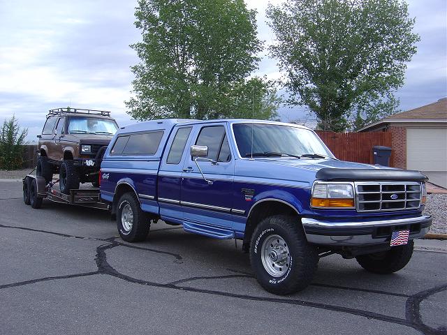 Blue 1995 Ford F-250 towing a lifted brown Ford Bronco II on a trailer