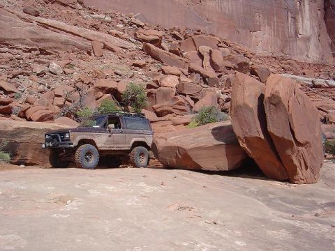 1986 Ford Bronco II - 1986 Ford Bronco II navigating a rocky off-road trail with large boulders nearby.