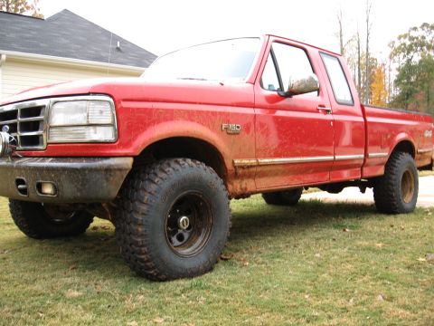 1995 Ford F-150 - Mud-splattered red Ford F-150 extended-cab 4x4 parked on grass, viewed from the driver's front three-quarter with dried mud sprayed up the…