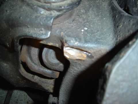 1986 Ford Bronco - Close-up underside view of a greasy cast-iron steering knuckle or axle component, showing dark metal surfaces with a fresh scrape or gouge…