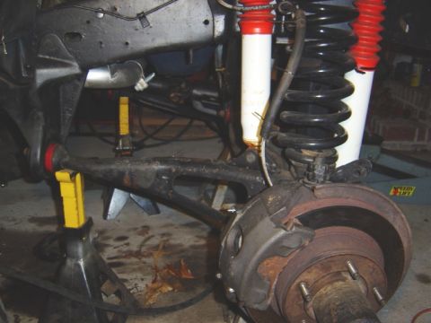 1986 Ford Bronco - Close-up of a vehicle's front suspension and brake system, supported by jack stands.