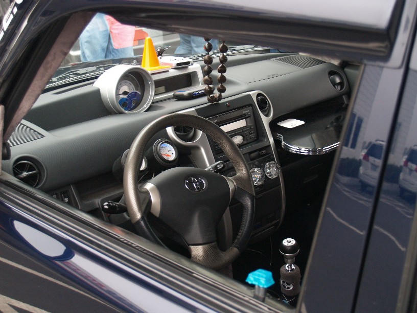 Car interior showing dashboard, steering wheel with Toyota logo, aftermarket gauges, and gear shifter