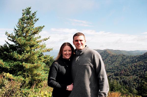 Couple posing for a photo with a pine tree and mountains in the background