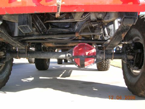 1985 Ford Bronco - The underside of a red vehicle is shown, focusing on the rear axle and differential. Another vehicle is partially visible in the background.