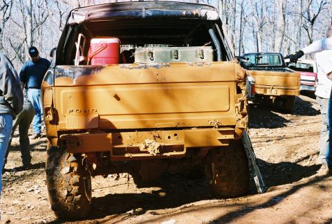 1978 Ford Bronco - A muddy 1978 Ford Bronco is viewed from the rear, with other vehicles and people in the background.