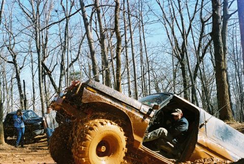 1978 Ford Bronco - Muddy 1978 Ford Bronco stuck during off-roading event, with another vehicle and spectators nearby.