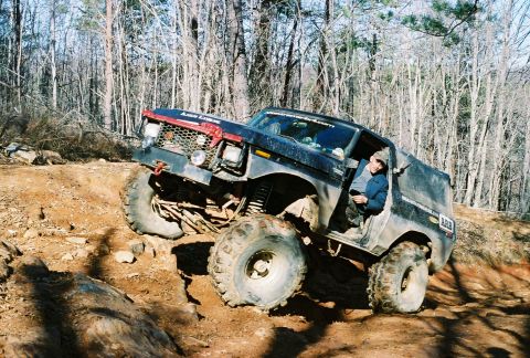 1978 Ford Bronco - A modified 1978 Ford Bronco navigates a steep, rocky incline in a wooded area.