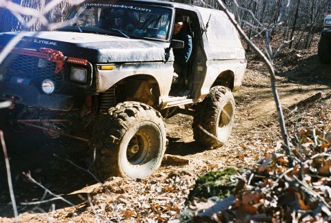 1978 Ford Bronco - A heavily modified 1978 Ford Bronco navigates a wooded trail with large off-road tires.