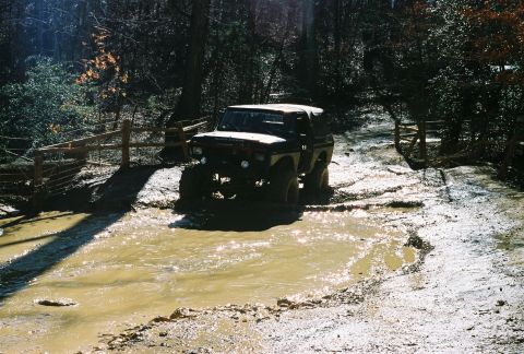 1978 Ford Bronco - A 1978 Ford Bronco navigates a challenging muddy terrain in a wooded area.