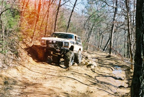 1978 Ford Bronco - A lifted Ford Bronco navigates a challenging off-road course through a wooded area.