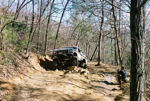 1978 Ford Bronco - Off-road vehicle tackles a challenging muddy trail in a wooded area.