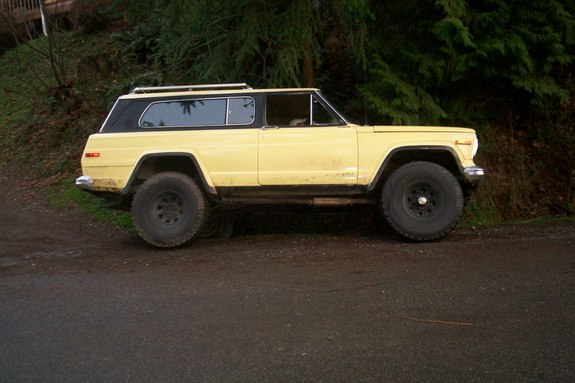 Yellow Jeep Cherokee SJ with black roof and large tires, parked on a dirt road