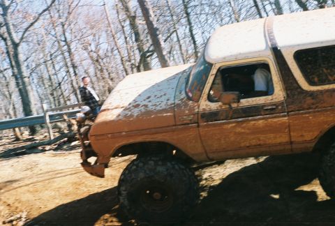 1978 Ford Bronco - A muddy 1978 Ford Bronco drives off-road through a wooded area.