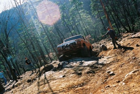 1978 Ford Bronco - Orange 1978 Ford Bronco navigates a challenging off-road course with spectators watching.