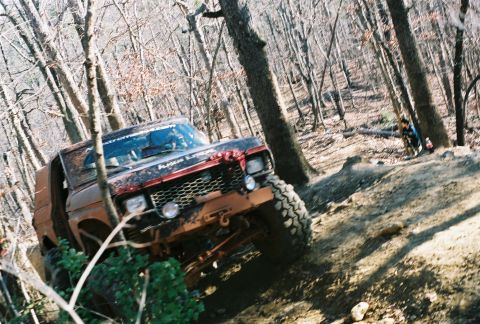 1978 Ford Bronco - A muddy 1978 Ford Bronco navigates a steep, wooded trail.
