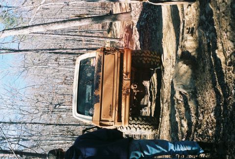 1978 Ford Bronco - A muddy 1978 Ford Bronco is seen from the rear in a wooded, off-road environment.