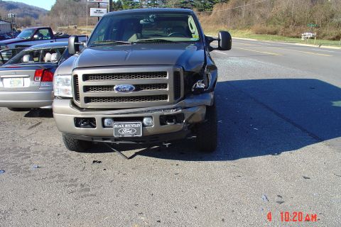2002 Ford Excursion - A Ford Super Duty truck with front-end damage sits on the road next to another vehicle.