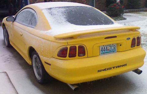 1998 Ford Mustang - A yellow 1998 Ford Mustang is covered in snow and ice, with icicles hanging from the rear bumper.