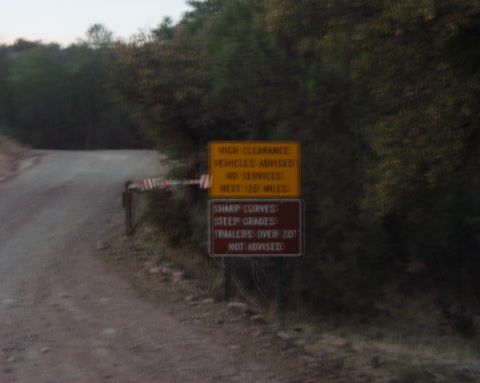 1997 Ford F-250 - Two signs on a dirt road provide warnings for drivers regarding vehicle clearance, services, road conditions, and grades.