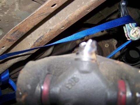 1995 Ford Bronco - Ratchet strap is used to secure a component on the underside of a vehicle.