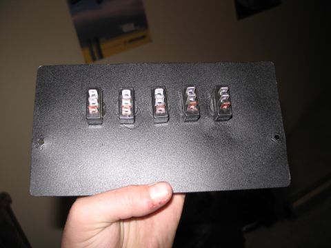 1995 Ford Bronco - A hand holds a black panel with five toggle switches mounted on it.