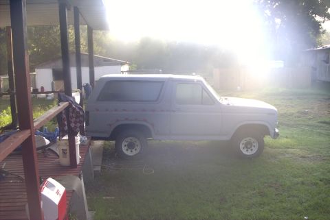 1984 Ford Bronco - This gray Ford Bronco, likely from the 1980s, is parked in a grassy area next to a covered porch.