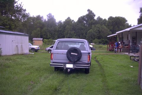 1984 Ford Bronco - Rear view of a 1984 Ford Bronco parked in a grassy yard with another vehicle visible.