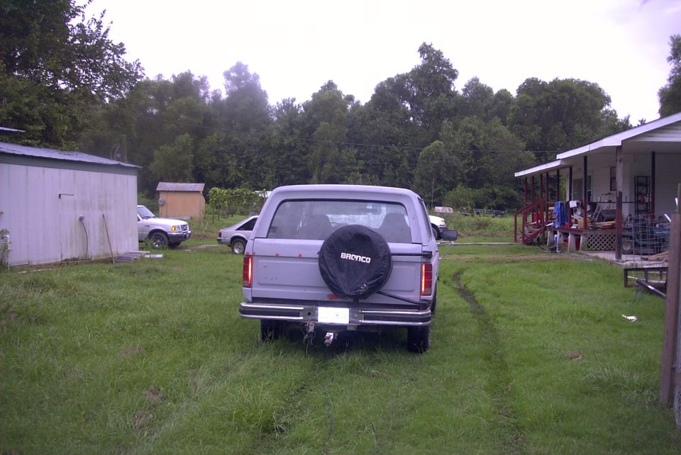 Rear of gray Ford Bronco on grass with black BRONCO spare tire cover and chrome bumper