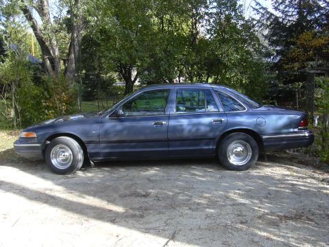 1996 Ford Crown Victoria - This 1996 Ford Crown Victoria is shown from the side, parked on a dirt area with trees in the background.