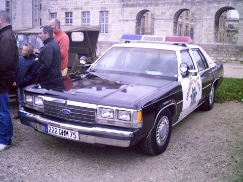 1991 Ford Crown Victoria - A police car with 'Highway Patrol' markings is parked next to other vehicles in front of a stone building.