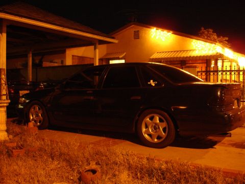 1993 Ford Taurus - A black 1993 Ford Taurus sedan is parked in a driveway at night, illuminated by house lights.